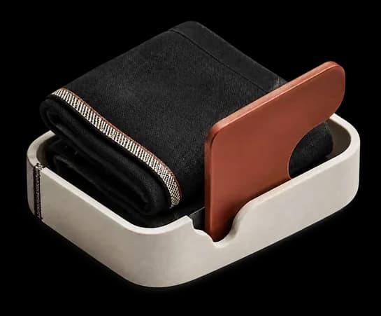 An open ivory box holding folded denim and a clay card